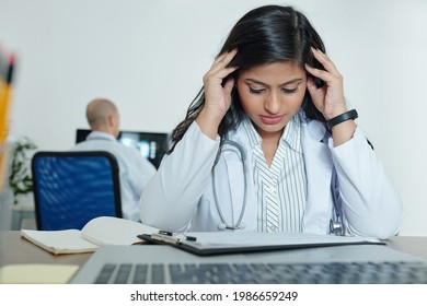 Stressed Young General Practitioner Trying To Concentrate On Work When Reading Medical History Of Patient