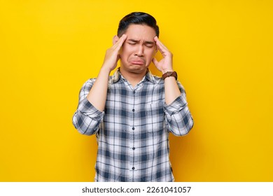 Stressed young handsome Asian man wearing casual clothes touching her temples and having headaches isolated on yellow background. People lifestyle concept
