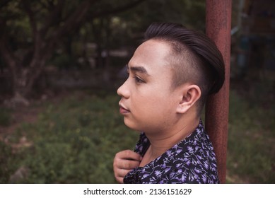 A stressed young man in deep thoughts. Walking around the park. Wearing a patterned shirt. Bothered by bills, self-esteem and relationship problems.