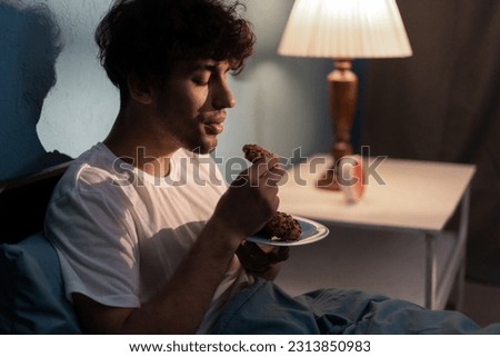 Stressed young man having a cookies at night. Unhappy tired depressed person eating during nighttime. Insomnia concept