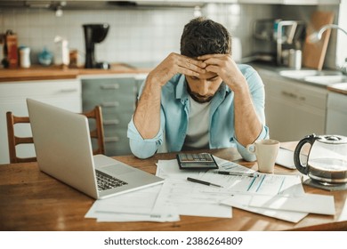 Stressed young man managing debt in kitchen