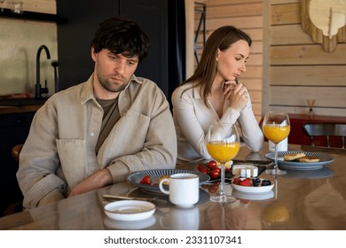 Stressed young married couple sits separately on opposite sides of the dining table, ignoring each other after a quarrel. Offended spouses do not talk, communicate, feeling depressed and disappointed - Shutterstock ID 2331107341