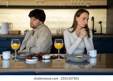 Stressed young married couple sits separately on opposite sides of the dining table, ignoring each other after a quarrel. Offended spouses do not talk, communicate, feeling depressed and disappointed - Shutterstock ID 2331107501