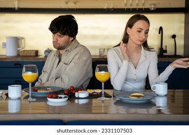 Stressed young married couple sits separately on opposite sides of the dining table, ignoring each other after a quarrel. Offended spouses do not talk, communicate, feeling depressed and disappointed - Shutterstock ID 2331107503