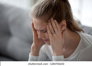 Stressed young sick woman having strong terrible headache suffering from chronic migraine or high blood pressure tension massaging temples to relieve head ache pain, tired exhausted girl feeling hurt