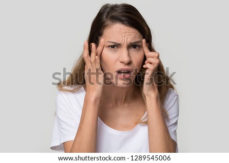 Stressed young woman confused about facial wrinkles aging skin on forehead or crows feet looking at camera isolated on studio background, upset worried girl having headache touching temples, portrait
