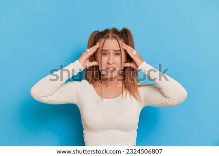 Stressed young woman covering her ears with hands and looking at camera isolated over blue background