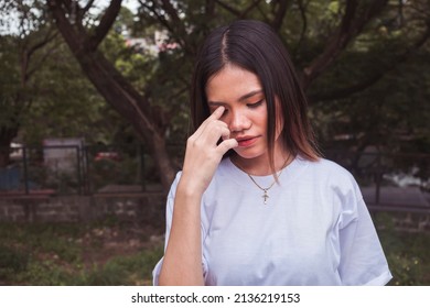 A stressed young woman in a plain white shirt deep thoughts. Wearing a white shirt. Bothered about the bills, self-esteem and relationship problems. Standing outside the park.