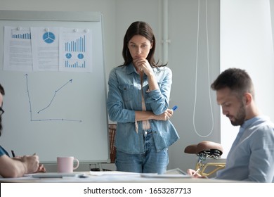 Stressed young woman standing near flipchart, feeling nervous before presentation. Thoughtful female brunette speaker touching chin, remembering or repeating mentally speech before performance. - Shutterstock ID 1653287713