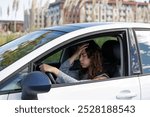 Stressed young woman stranded in the middle of the road because her car broke down. She calls for help on her phone, waiting for the tow truck. Roadside assistance. Reflective vest and triangle.