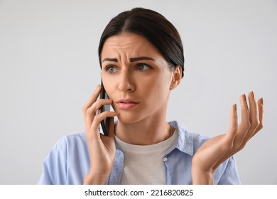 Stressed young woman talking by mobile phone on light background - Powered by Shutterstock