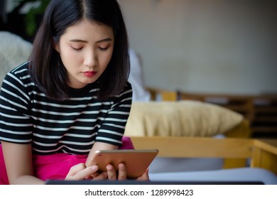 Stressed young woman using tablet computer in Coffee shop. Asian female sitting on couch using tablet ipad surfing, reading message, internet information in cafe.