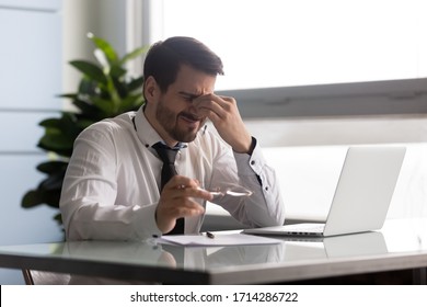 Stressful businessman taking off glasses, suffering from dry eyes syndrome after long laptop use. Exhausted employee executive manager ceo feeling eye strain, massaging nose bridge - Powered by Shutterstock