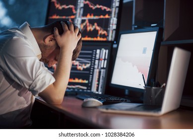 Stressful day at the office. Young businessman holding hands on his face while sitting at the desk in creative office. Stock Exchange Trading Forex Finance Graphic Concept.