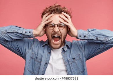 Stressful hipster male scremas in panic, closes eyes in terror, keeps hands on head, finds out terrified news or disaster about best friend, can`t believe of his death. People, stress, annoyance - Shutterstock ID 748837381