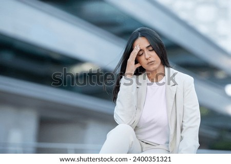 Stressful Job. Stressed Hispanic Businesswoman Touching Head Having Headache Problem, While Sitting Outside Of Modern Corporate Building, Having Issues At Workplace. Empty Copy Space For Text