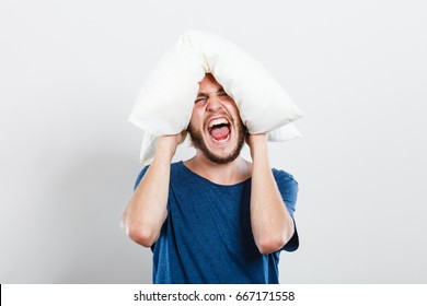 Stressful unpleasant situation conflict. Angry mad young man closing ears with pillow, protecting from loud noise. Guy not wanting to listen or can not fall asleep