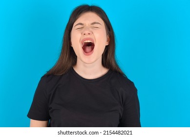 Stressful Young Caucasian Woman Wearing Black T-shirt Over Blue Background Screams In Panic, Closes Eyes In Terror, Keeps Hands On Head, Finds Out Terrified News, Can't Believe It.