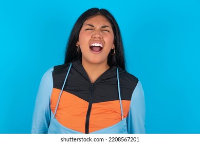 Stressful Young Latin Woman Wearing Sport Clothes Over Blue Background Screams In Panic, Closes Eyes In Terror, Keeps Hands On Head, Finds Out Terrified News, Can't Believe It.