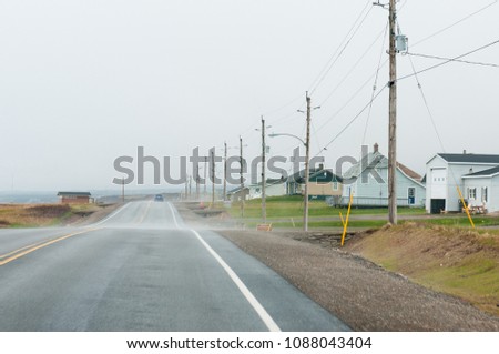 Stretch of empty road with houses and telephone poles and wire to the right along the Cabot Trail, Cape Breton, Canada