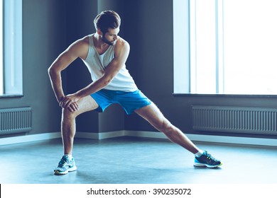 Stretching After Great Work Out. Young Handsome Man In Sportswear Doing Stretching At Gym