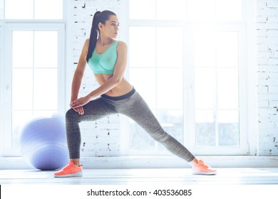 Stretching after great workout. Young beautiful young woman in sportswear doing stretching while standing in front of window at gym