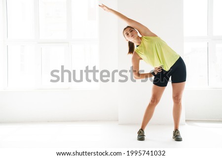 Stretching after great workout. Young beautiful young woman in sportswear doing stretching while standing in front of window