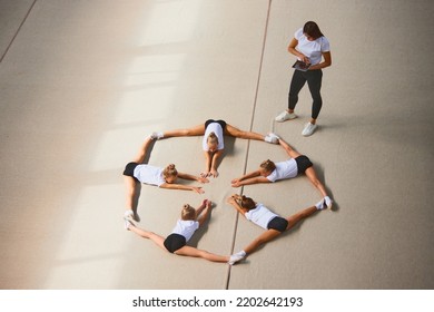 Stretching, Flexibility Exercises. Aerial View. Female Sports Coach Training Gymnastics Athletes At Sports Gym, Indoors. Concept Of Achievements, Studying, Goals. Coaching, Training, Psychology