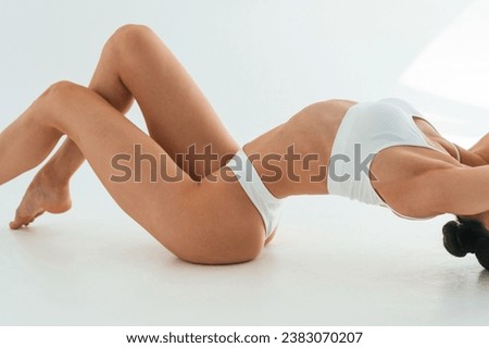 Stretching on the floor, close up view. Young woman with slim body type is in fitness clothes in the studio.
