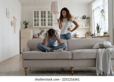 Strict mother scolding unhappy teenage daughter at home, mom lecturing teen girl, child sitting on sofa feeling afraid covering ears with hands. Parental harsh discipline, adolescent problem behavior  - Powered by Shutterstock