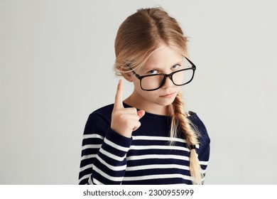 Strict, serious and portrait of a child with a gesture isolated on a white background in a studio. Rude, smart and a young girl wearing glasses and gesturing with finger for discipline on a backdrop