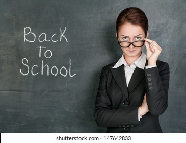 Strict Teacher On The School Blackboard Background With Phrase Back To School