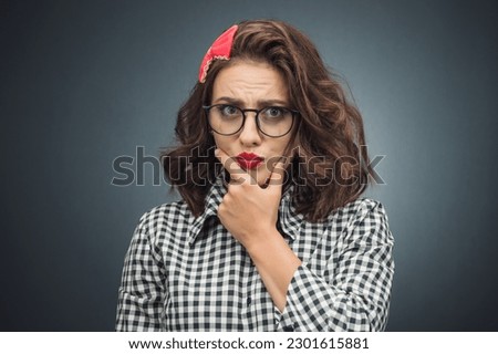 Strict woman with hand on chin looking at angry face expression over dark gray - black background. Jealous woman with doubt expression. Studio shot