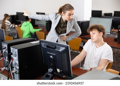 Strict young female teacher reprimanding negligent teenage student sitting at computer in classroom during lesson.. - Powered by Shutterstock