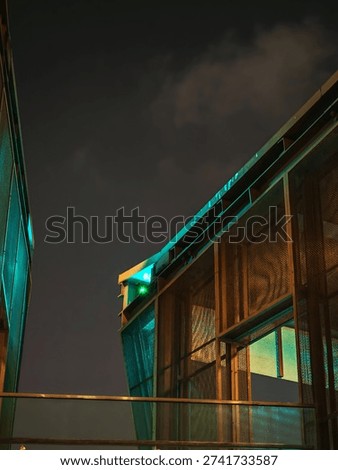 A striking, angular building with teal windows dominates a dark Hong Kong night, reflecting the city's innovative transformation.