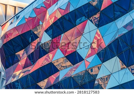 Striking architectural facade composed of triangular panels, reflecting vibrant colors and urban environment, showcasing dynamic geometric patterns with interplay of light and shadow