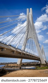 A striking architectural marvel, this cable-stayed bridge dominates the landscape under a bright blue sky dotted with fluffy clouds, showcasing its intricate design and engineering prowess