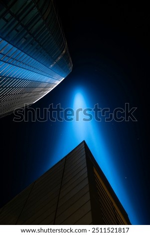 A striking beam of light illuminates the night sky above modern skyscrapers in an urban setting, showcasing cutting-edge architectural design in a vibrant city landscape