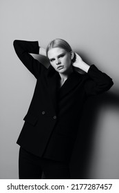 A Striking Blonde Girl In A Classic Suit Holds Her Hair With Her Hands And Poses Like A Professional Model In A Studio In Black And White Style. Fashion Photography. Concept For Clothing Stores