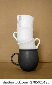 Striking composition of kitchenware: a sturdy black mug serves as the base for a precarious stack of three glossy white cups.