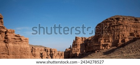 a striking formation of red sandstone cliffs set against a clear azure sky, their rugged textures highlighted by the sunlight, suggesting a peaceful desert scene in daylight