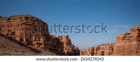 a striking formation of red sandstone cliffs set against a clear azure sky, their rugged textures highlighted by the sunlight, suggesting a peaceful desert scene in daylight