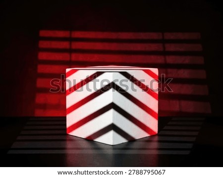 A striking geometric cube featuring a bold chevron pattern of white and black stripes, illuminated by a dramatic red backlight.
