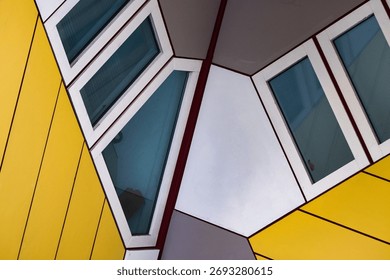 Striking geometric window frames in bold yellow and teal colors create a dynamic architectural composition against a cloudy sky.