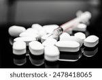 A striking image capturing a collection of white pills alongside a syringe, set against a reflective black backdrop, portraying medical treatment and health interventions, opioids and fentanyl use. 