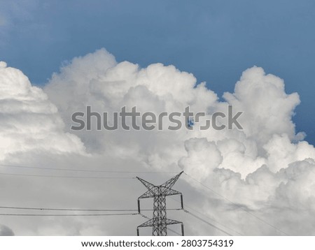 A striking image capturing the immense scale of cumulonimbus clouds with a power line tower silhouetted against them.