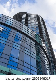 A striking low angle perspective looking straight up the facade of a tall, modern curved glass skyscraper reflecting the blue sky. The scene represents corporate ambition, towering real estate, and modern structural engineering.
