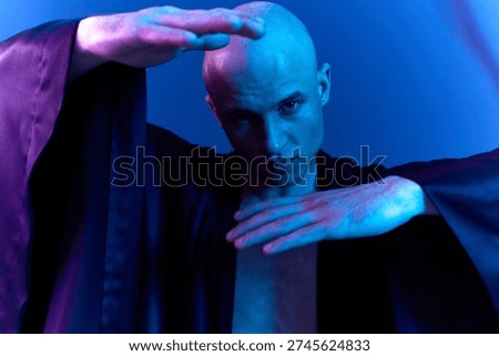 Striking man in a dramatic pose, showcasing artistry with illuminated colors in a mesmerizing black and white image. A captivating visual experience awaits viewers.