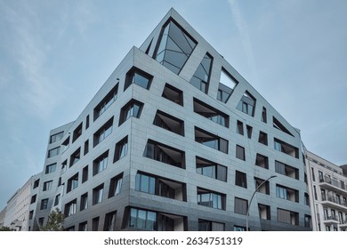 A striking modern building showcasing angular architecture with sharply defined geometric windows and sleek metallic exterior panels.