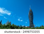 Striking modern wooden tower Pyramidenkogel reaching towards vibrant blue sky in Carinthia, Austria. Interconnected platforms and spiraling staircases that ascend to pointed observation deck. Landmark